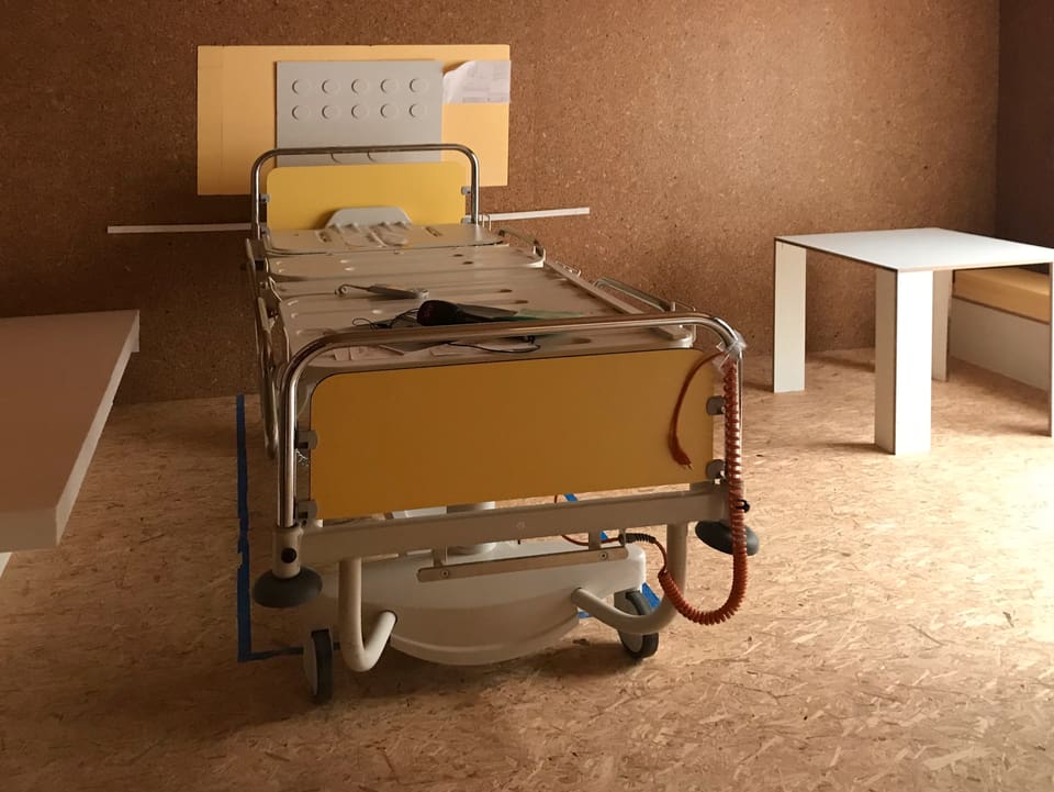 Ein Spitalbett steht in einer Holzbox, an der Wand die Simulation von verschiedenen Anschlüssen.