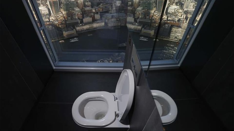 Toilette im Vordergrund vor grossem Glasfenster mit Blick über London.