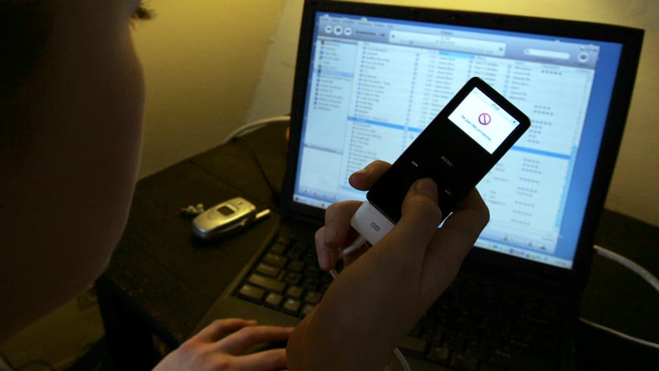 Eine Person vor einem Laptop, einen angeschlossenen iPod zum Musikhören in der Hand.