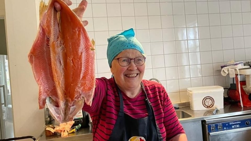 die nordschwedische slow-food-köchin Ingrid Pilto hält einen ausgenommenen, halbierten Fisch in die Luft und grinst