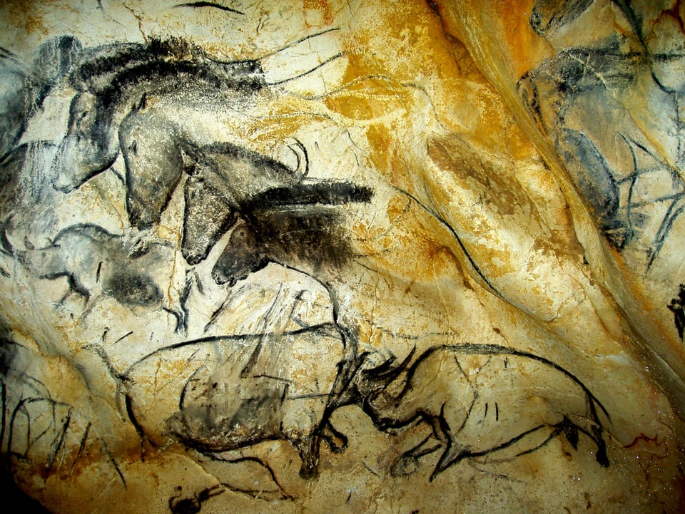 Kämpfende Nashörner, darüber eine Detailansicht von Pferdeköpfen. Die Skizzen sind schwarz, die Felswände gelblich.