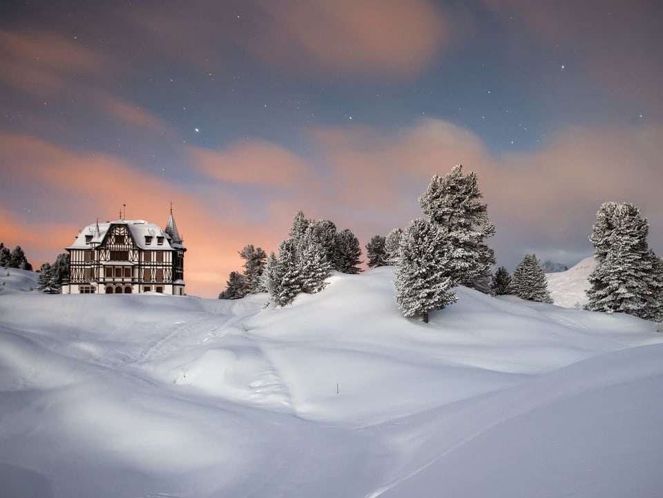 Blick auf eine verschneite Landschaft und ein Haus unter Sternenhimmel.