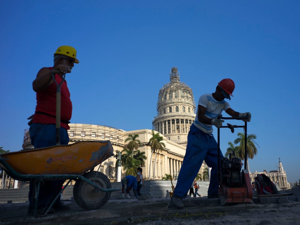 Zu sehen sind zwei Strassenarbeiter mit einer Schubkarre, welche eine Strasse in Havanna frisch teeren.