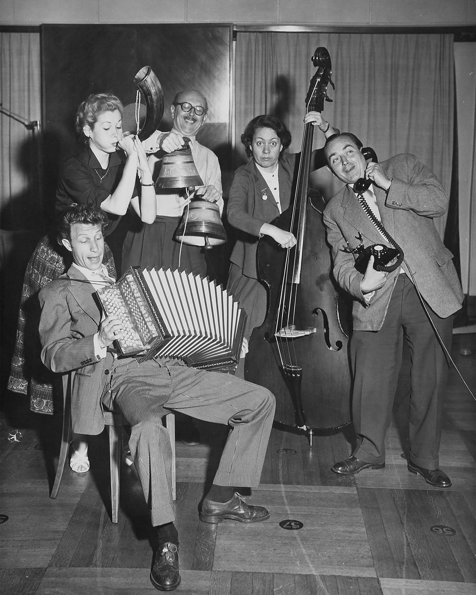 Schwarz-weiss Foto mit zwei Frauen und drei Männern, die fröhlich musizieren.