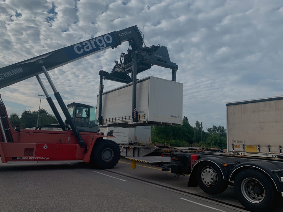 Ein Gabelstapler hebt einen Container von einem Lastwagen und stellt ihn auf einen Bahnwagen.