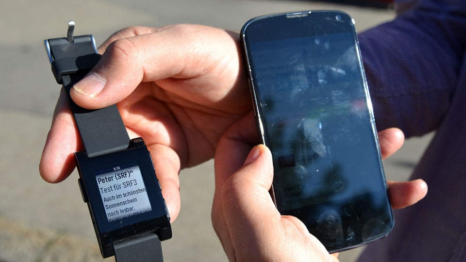 Eine Smartwatch neben einem Smatphone. Der Text auf der Smartwatch ist lesbar während der Bildschirm des Handys glänzt.