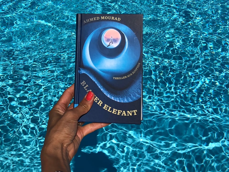 Annette König hält das Buch von Achmed Mourad: «Blauer Elefant» vor blaues Wasser