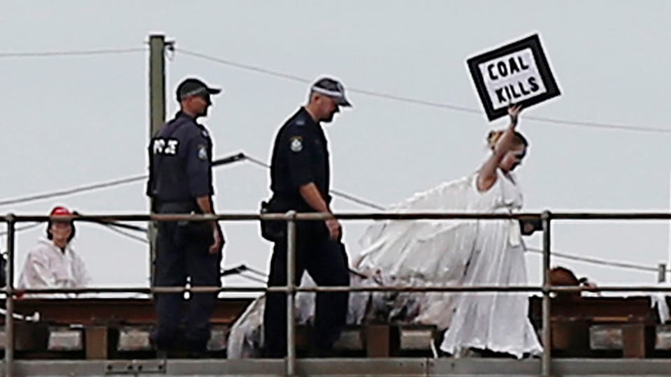 Eine Frau in einem weissen Kleid hält ein Schild «coal kills», sie wird von zwei Polizisten gefolgt.