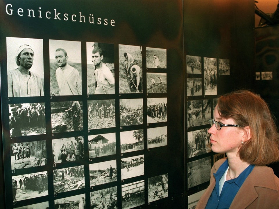 Eine Frau betrachtet Fotos in einer KZ-Ausstellung. Die Tafel heisst "Genickschüsse"