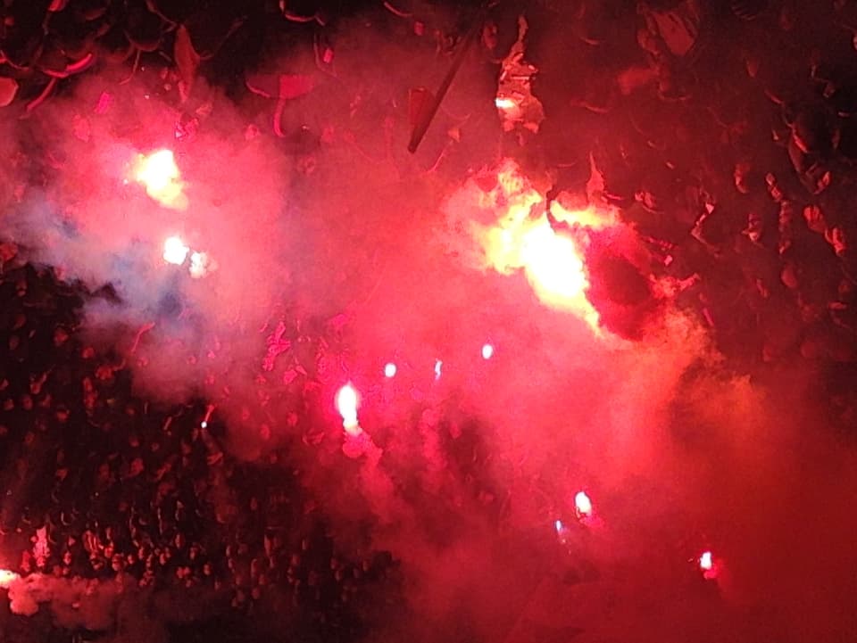 Fussballfans feiern ihre Mannschaft im roten Licht der Petarden.