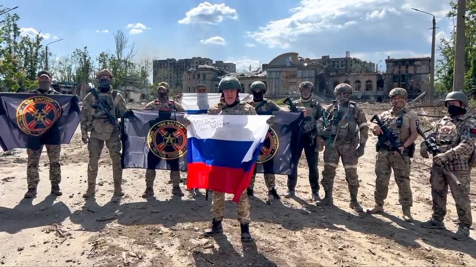 Prigoschin hält eine Russland Fahne. Dahinter mehrere Soldaten mit der Fahne der Gruppe Wagner