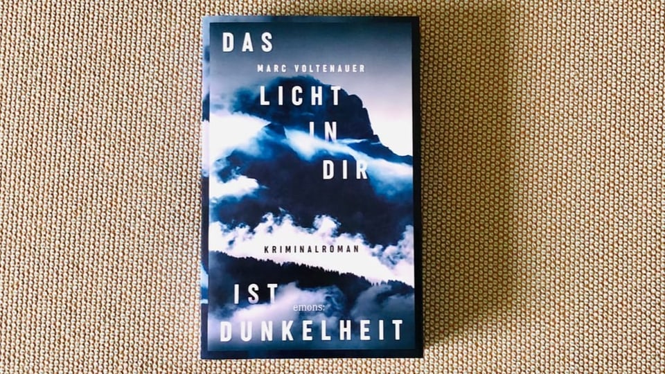 Krimi Nummer 4 «Das Licht in dir ist Dunkelheit» von Marc Voltenauer liegt auf einem beigen Sofastoff