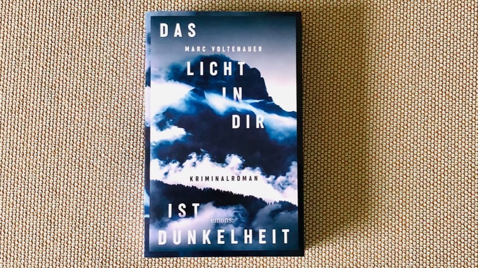 «Das Licht in dir ist Dunkelheit» von Marc Voltenauer liegt auf einem beigen Sofastoff