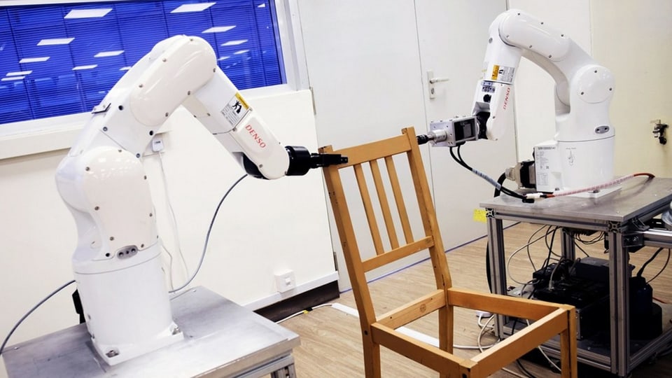 Zwei Roboter pecken mit ihren Armen an einen Stuhl.