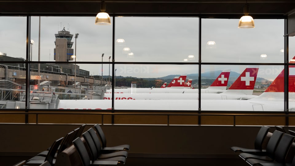 Blick aus einem Fenster des Flughafens Zürich auf stehende Flugzeuge.