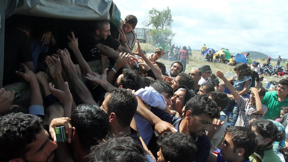 Flüchtlinge drängen sich um ein Fahrzeug und bitten um Wasser
