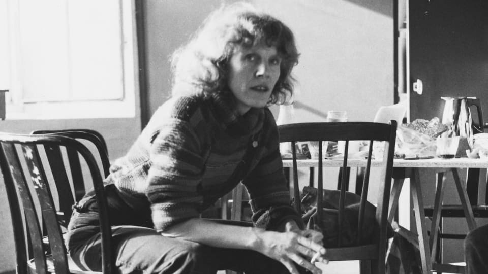 Frau in ihren Vierzigern sitzt an Esstisch und schaut in Kamera, Schwarzweissaufnahme