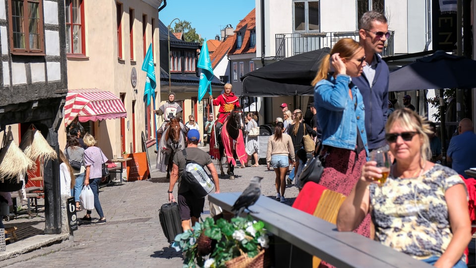 Touristen und zwei Ritter auf Pferden zwischen den historsichen Riegelhäusern in Visby/Gotland.