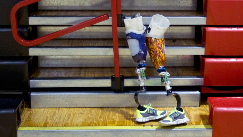 Zwei Beinprothesen mit Sportschuhen lehnen an einer Wand.