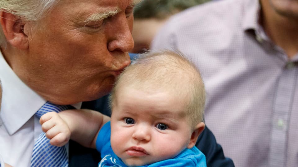 Trump küsst ein kleines Kind auf den Kopf, das er im linken Arm hält