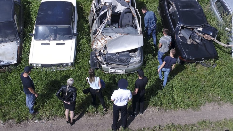 Fahrschülerinnen und -schüler betrachten Unfallautos