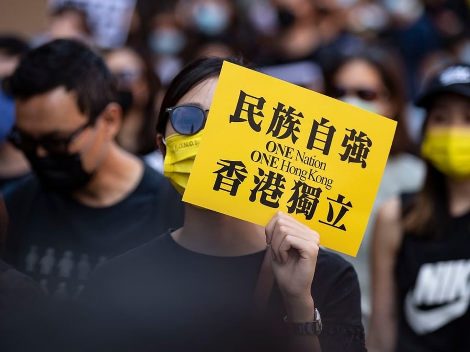 Menschenmasse. Eine Frau hält ein gelbes Schild hoch: «One Nation. One Hongkong.»