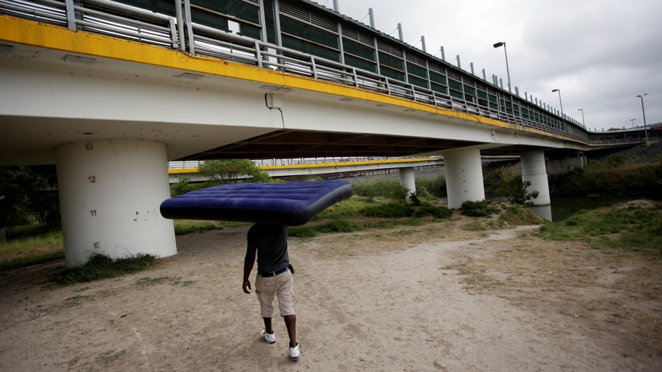 Mann trägt Matratze über dem Kopf in Richtung einer Brücke.