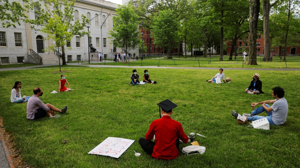 Studenten sitzen mit Maske auf Rasen