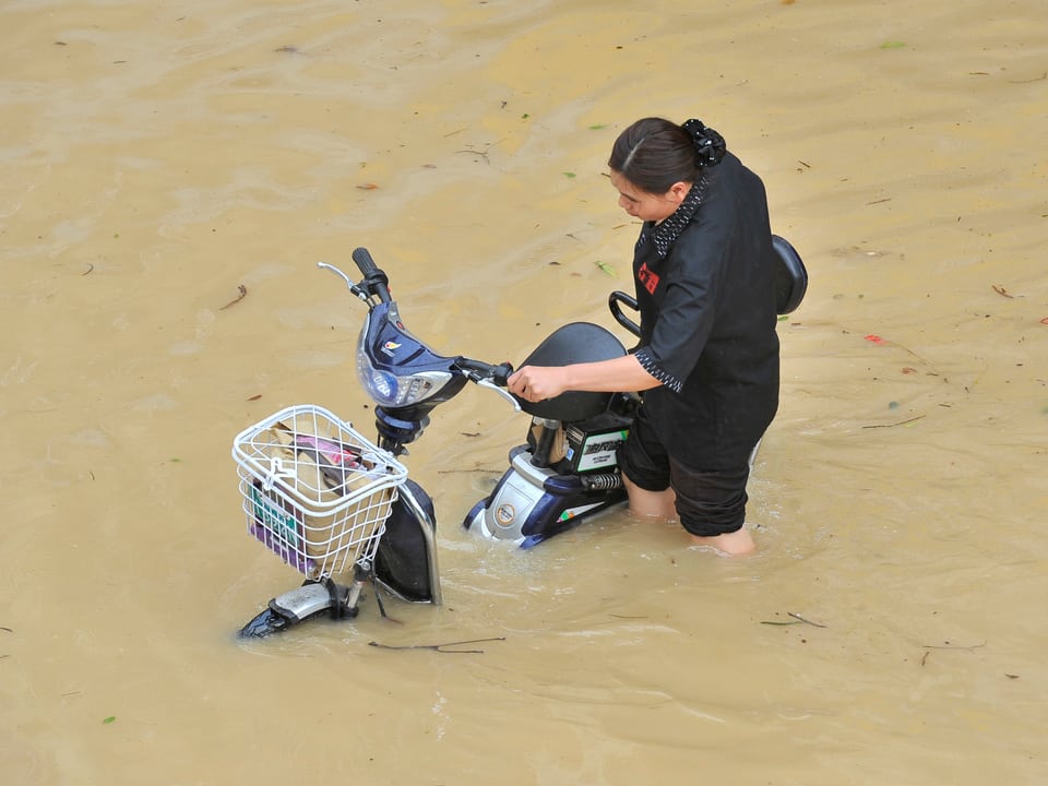 Frau schiebt Moped durch das Wasser.