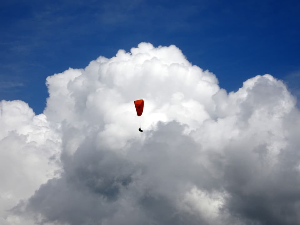 Ein Gleitschirmpilot fliegt vor einer mittelgrossen Gewitterwolke.