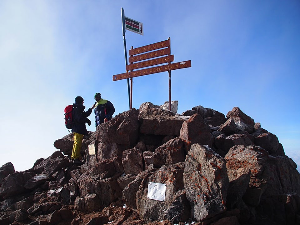 Blick auf den felsigen Gipfel, zwei Männer in Bergsteigermontour im Gespräch.