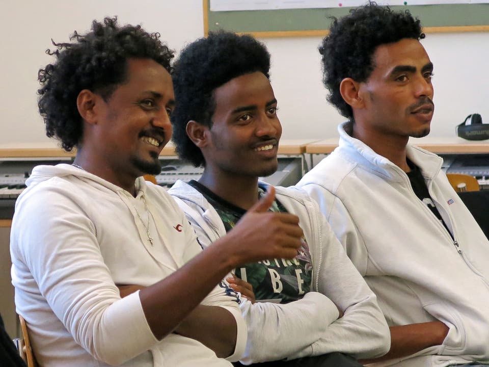 Drei Männer aus Eritrea sitzen nebeneinander und lachen.