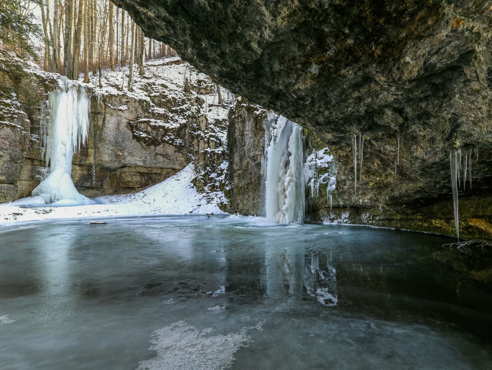 Zwei gefrorene Wasserfälle in einem verschneiten Wald.