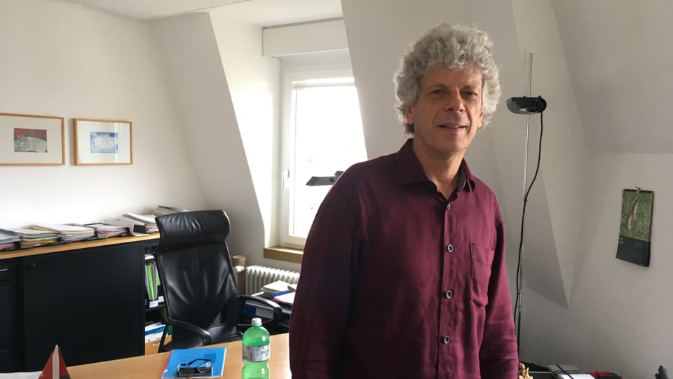 Porträt von Kreisschulpflege-Präsident Urs Berger in seinem Büro. Weisse Haare, rotes Hemd. 
