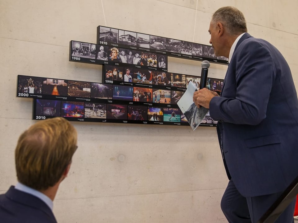 Zwei Männer sehen sich kleine Bilder an, die im Eingang der wieder eröffneten Halle angebracht sind.