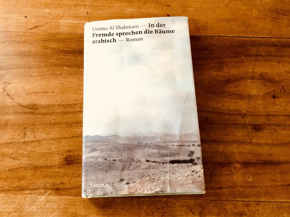 «In der Fremde sprechen die Bäume arabisch» von Usama Al Shahmani liegt auf einem blanken Holztisch 