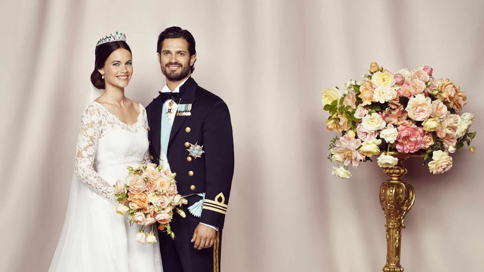 Das frisch vermählte Brautpaar posieren neben einem Blumenbouquet.