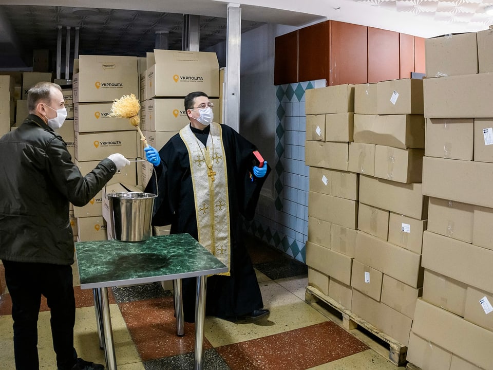 Priester besprenkelt Kisten mit Weihwasser