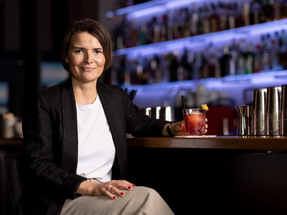 Frau in Blazer sitzt an Bar unt trinkt einen alkoholfreien Cocktail