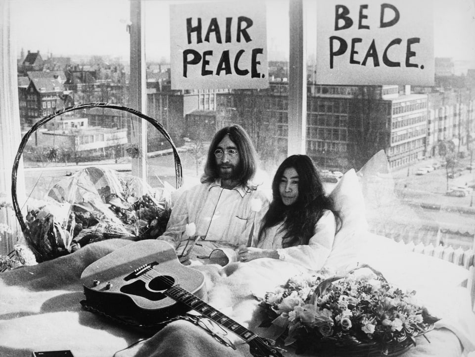 Lennon und Ono 1969 in einem Bett. Im Hintergrund Friedens Parolen. 