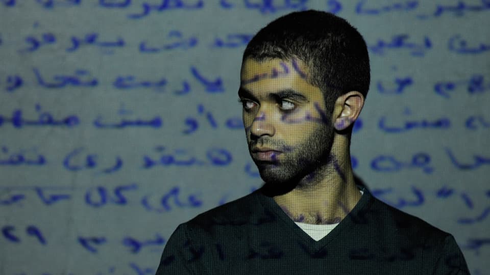 Projektion eines arabischen Textes auf eine Wand und den Körper eines davor stehenden Künstlers. 
