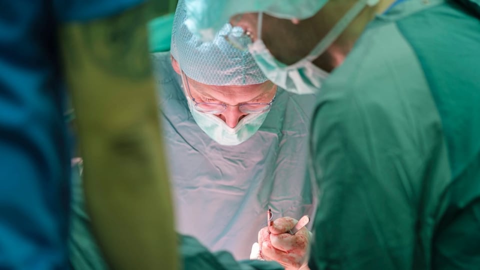 Ein Chirurg beugt sich während einer Operation über einen Patienten. Auf seinem Handschuh ist Blut. 