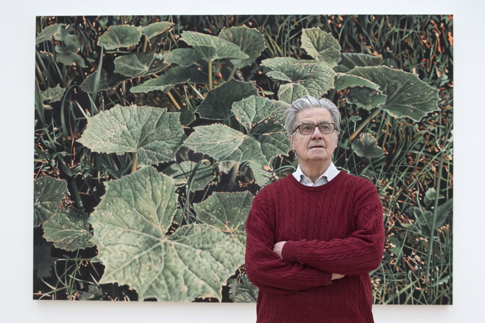 Älterer Herr in rotem Pulli posiert vor Pflanzen-Gemälde