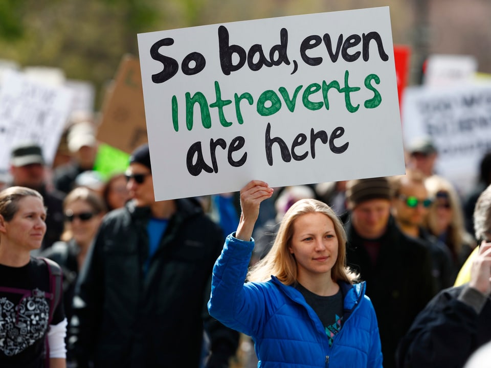Eine Frau hält an einem Protestmarsch ein Plakat auf dem steht: «So bad, even introverts are here.»