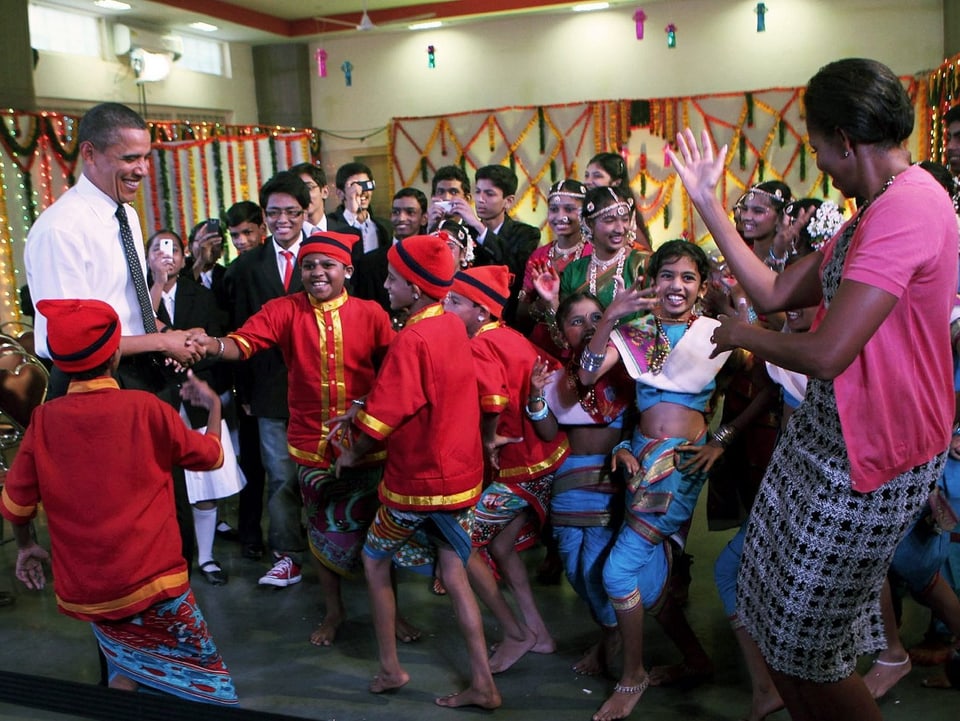 Barack Obama und Michelle tanzen umzingelt von Kindern in einer indischen Schule.
