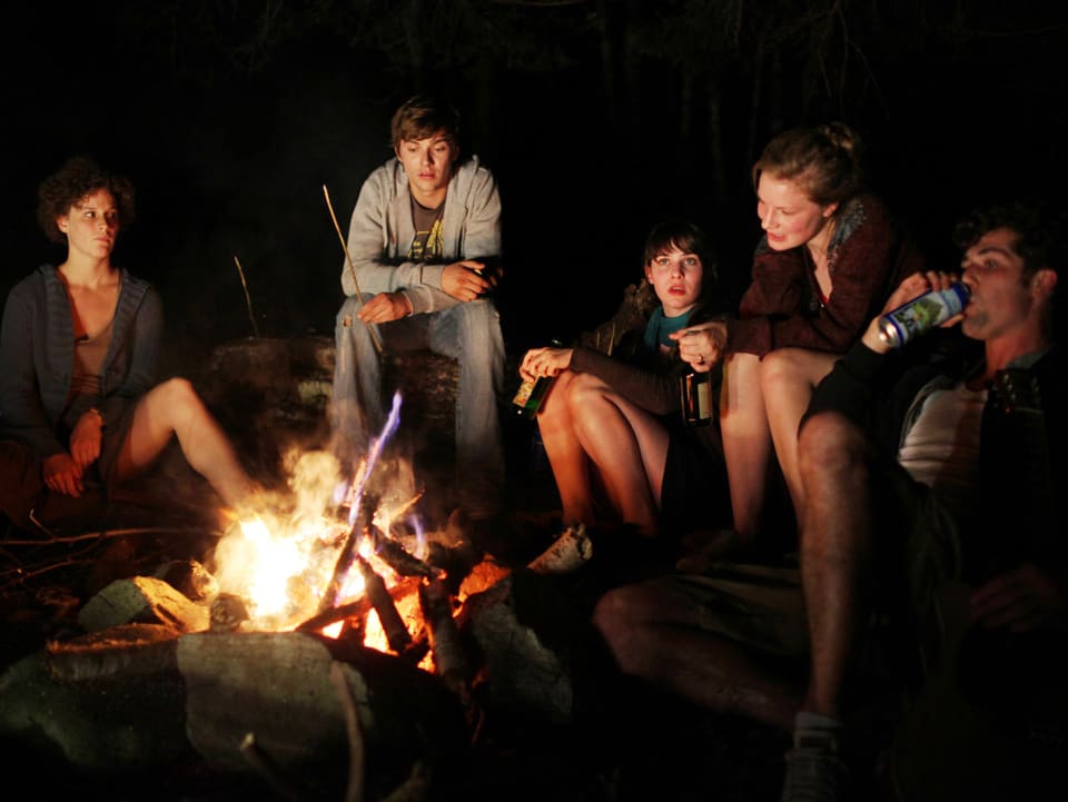 Eine Gruppe junger Menschen sitzt am Lagerfeuer.