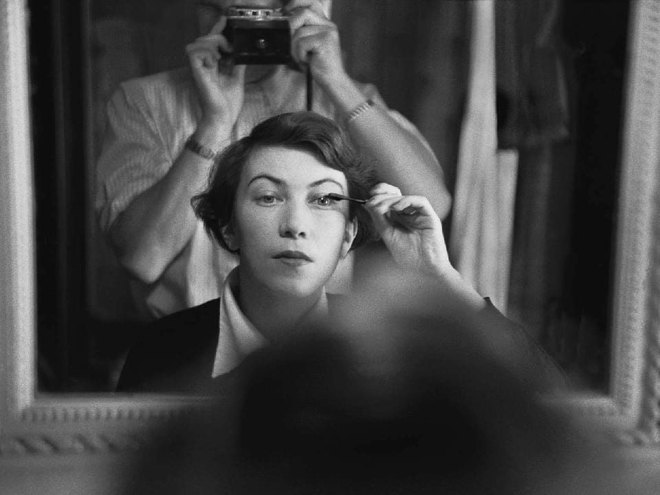 Ein Frau sitzt vor dem Spiegel und schminkt sich. Der Fotograf ist im Spiegelbild stehend hinter ihr erkennbar.