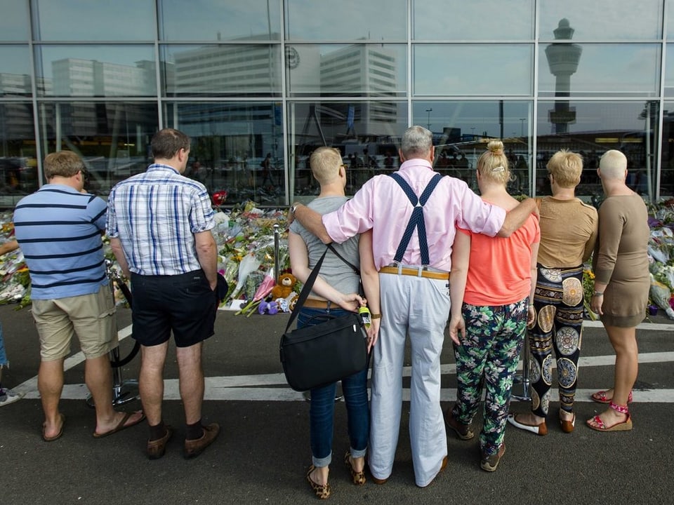 Niederländer, die in diesen Tagen von Amsterdam aus in die Ferien fliegen, halten beim Blumendenkmal am Flughafen Schiphol inne.