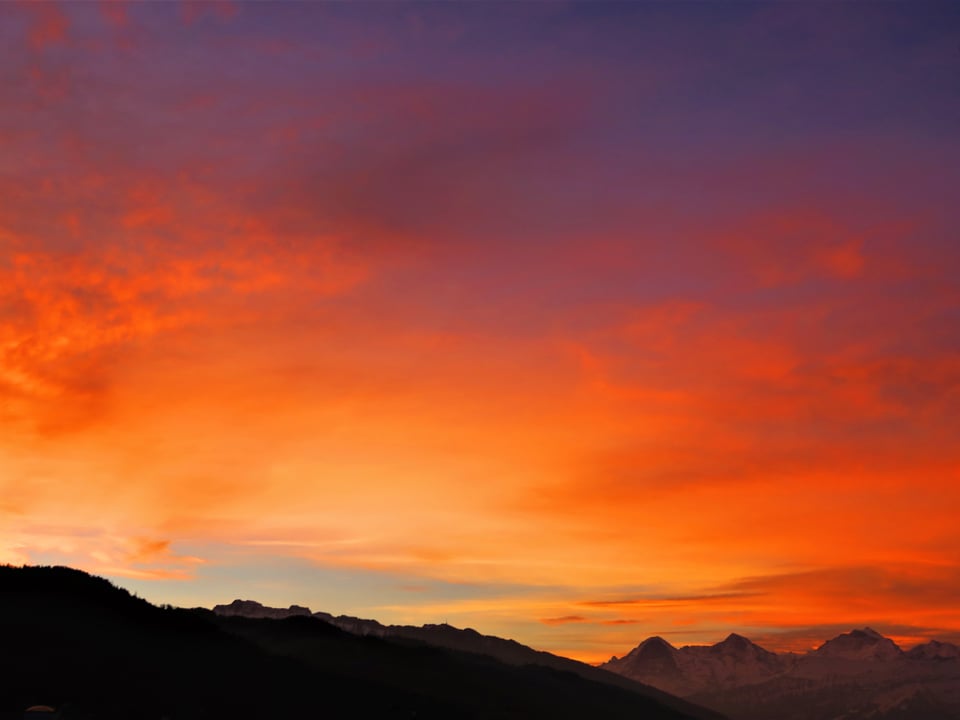 Rötlich verfärbter Himmel mit vielen Wolkenfeldern, im Hintergrund die verschneiten Berner Alpen.