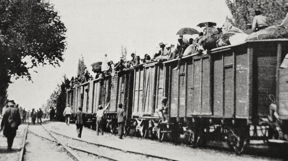 Historische Fotoaufnahme, auf der Güterwägen voll beladen mit flüchtenden Menschen zu sehen sind.